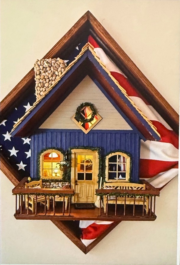 A blue cottage with a miniature balcony and illuminated windows, framed by an American flag — the build where Justin found his thing.