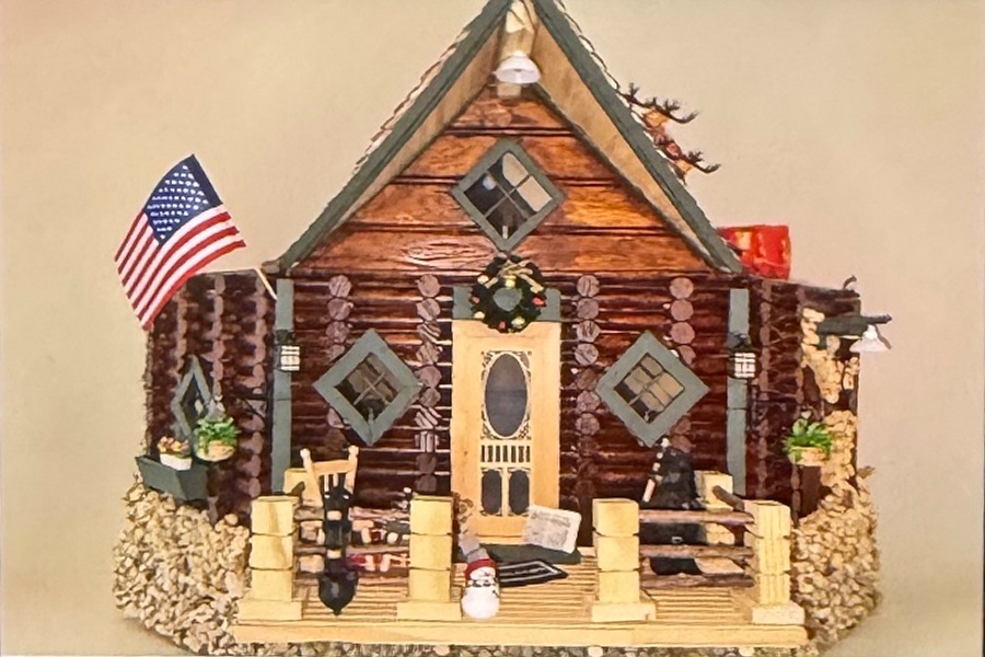 A rustic log cabin with a detailed porch, stone foundation and American flag — a wall-mounted cat house, and Justin’s first completed build.